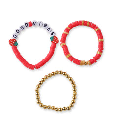 Flat lay of Berry Bliss Clay Bead Bracelet Stack - includes red clay beads, gold beads, and a 'Good Vibes' bracelet with strawberry charms.