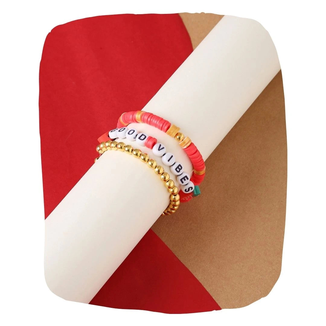 Clay Bead Bracelet Stack - Berry Bliss set of 3 featuring vibrant red, gold, and 'Good Vibes' letter beads, wrapped around a display roll.