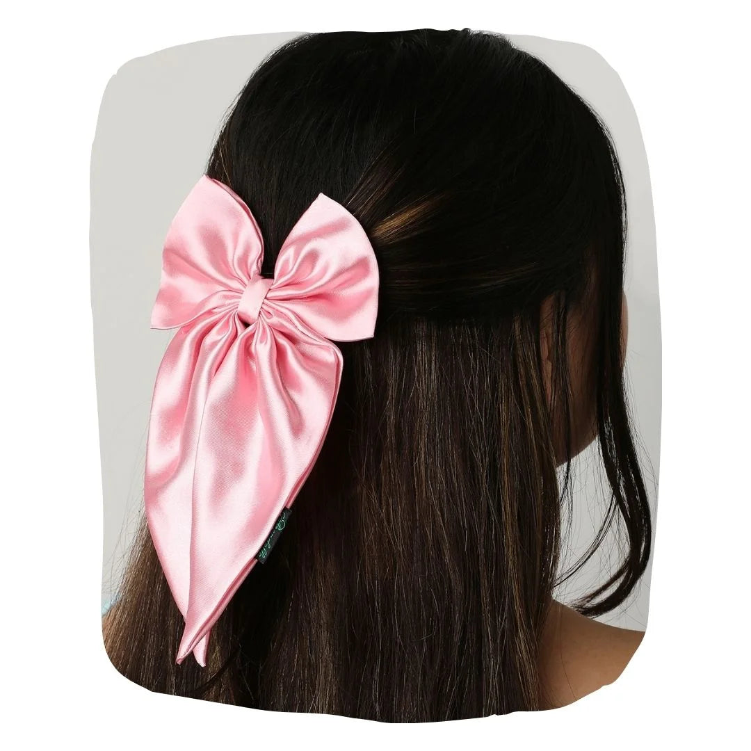Pink handmade satin hair bow with anti-breakage clip, styled on long dark hair for an elegant and charming look.