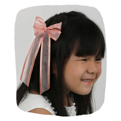 Handmade organza hair bow in pink worn by a smiling girl. Elegant and secure clip ideal for kids' hairstyles and special occasions.