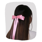 Pink satin silk ribbon bow styled on long dark hair. This XXL hair bow adds a vibrant, elegant touch to any hairstyle with a secure fit.
