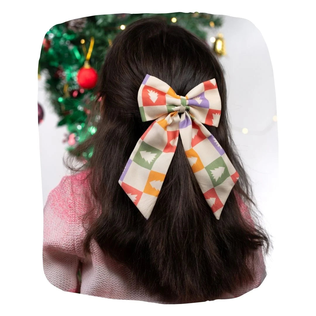 Girl wearing Arendelle Christmas hair bow with festive tree pattern in front of decorated holiday tree. Secure clip fits all ages.
