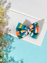 Christmas Gift Hair Bow in green with red, yellow, and pink present prints, styled flat on a white textured surface for festive accessory display.