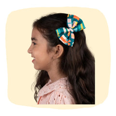 Girl wearing Christmas Gift Hair Bow in festive green with colorful present prints, perfect for holiday-themed hair accessories for kids.