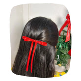 Girl wearing red Christmas hair bow by Arendelle with long ribbon tails, perfect festive accessory for holiday outfits.