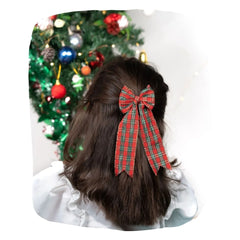 Girl wearing Arendelle Christmas Hair Bow in red and green plaid with secure clip, styled for festive holiday look near Christmas tree.