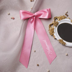 Pink satin bridesmaid bow with script text, ideal for wedding decor and hair styling. Elegant and reusable accessory for bridal parties.