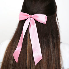 Bright pink satin Bride Tribe hair bow styled on half-up hairstyle, a trendy wedding accessory for bridal parties.