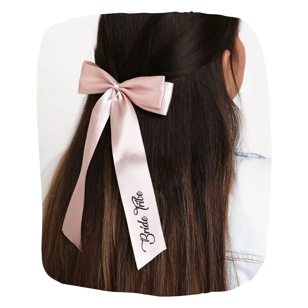Blush pink satin Bride Tribe hair bow clipped on long brown hair, ideal for bridal party styling and wedding accessories.