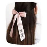 Blush pink satin Bride Tribe hair bow clipped on long brown hair, ideal for bridal party styling and wedding accessories.