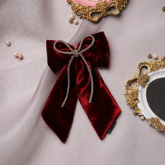Maroon velvet hair bow with rhinestone cord displayed on soft fabric with decorative frames, ideal for gifting or styling.