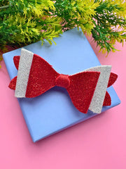 Red and silver glitter festive hair bow placed on blue gift box, styled for Christmas-themed accessories.