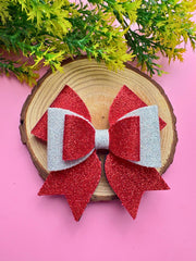Red and silver Christmas glitter hair bow displayed on a wooden slice with pink background. Stylish and trending holiday hair accessory.