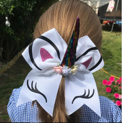 Girl wearing white Unicorn Cheer Bow featuring sequin horn and printed lashes. Ideal 7-inch hair accessory for girls aged 3 to 12.