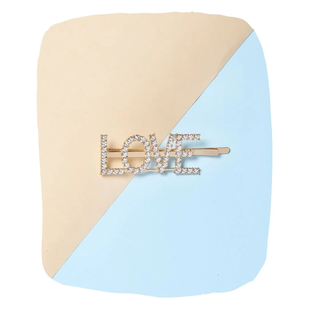 Gold 'LOVE' hairpin for kids with glitter rhinestones, displayed on a pastel beige and blue background. Stylish accessory for girls aged 3-10.