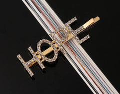 Close-up of Gold Glitter HOPE Hairpin on black surface, highlighting crystal embellishments and sturdy metal clip for secure hold.