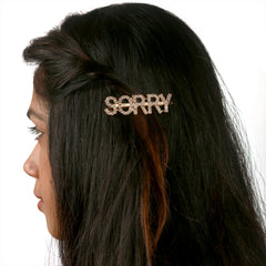 Trendy Gold Glitter Hairpin for Kids styled in dark hair. The 'SORRY' clip adds a fun and fashionable touch to any hairstyle.