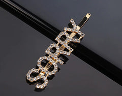 SORRY Clip - Gold Glitter Hairpin for Kids on a glossy black surface. Stylish and playful hair accessory with sparkling crystal details.