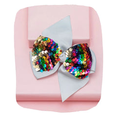 Stylish grey bow pin for girls with multicolor sequins, displayed on a pink gift box. A trendy hair accessory for special occasions.