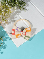 Soft stretchable Yellow Bow Baby Headband with pastel Christmas tree design, laid flat on a textured surface with floral decor.