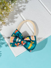 Soft and stretchable Christmas baby headband with green gift-print bow, displayed on a white textured surface under natural light.