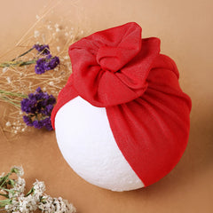 Shiny Dark Red Baby Turban Cap displayed on mannequin head with floral decor, showcasing soft texture and chic knotted top.