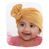 Shiny mustard baby turban cap made of soft cotton, worn by a smiling baby girl. Ideal for newborns and toddlers, perfect for everyday wear.