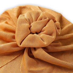 Close-up of the soft and stretchable cotton fabric of the shiny mustard baby turban cap, highlighting the elegant knotted flower design.