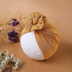 Cotton baby turban cap in shiny mustard displayed on a white mannequin head. Breathable and stretchable, great for stylish baby outfits.