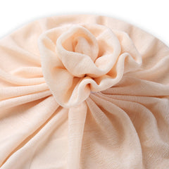 Close-up of Beige Baby Turban Cap flower knot detail. Soft, shiny fabric with elegant pleats for stylish baby wear.