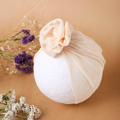 Shiny Beige Baby Turban Cap displayed on a mannequin head with floral decor. Breathable and stretchable cotton for toddlers.