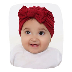 Baby wearing a maroon cotton bow turban cap, ideal for newborns. Ultra-soft and trendy hair accessory for 0 to 2 years in apparel category.