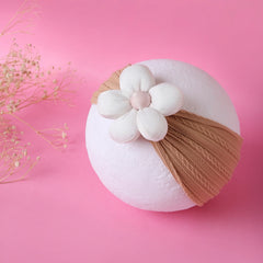 Tan baby cotton headband with plush white flower displayed on a round prop, perfect for newborns and toddlers. Soft, stretchable, and cute.