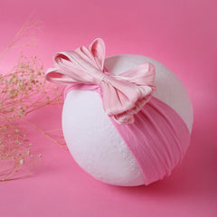 Soft pink baby cotton headband with large bow displayed on white ball. Stretchable, breathable fit for newborns and toddlers.