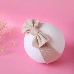 Light brown cotton baby headband with ribbed texture and bow knot displayed on a white sphere against a pink background.