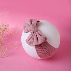 Light pink cotton baby headband with bow displayed on white mannequin ball. Soft and stretchy design for newborns and toddlers.