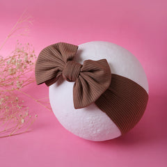 Brown soft cotton baby headband with bow displayed on a white mannequin ball against pink background. Trendy design for infants and toddlers.