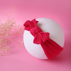 Dark pink cotton baby headband with big bow displayed on white sphere. Soft, stretchable accessory for baby girls.