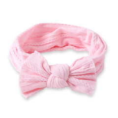 Light pink baby cotton bow headband laid flat to showcase its soft, breathable fabric and cozy stretch fit for newborns to toddlers.