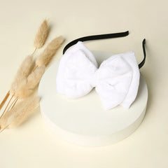 White velvet double layered bow hairband displayed on a round pedestal. Elegant and trendy hair accessory for girls.