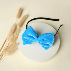 Blue velvet bow hairband displayed on a round white platform with soft dried grass, showcasing its elegant and trendy look.