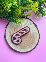 Festive Glitter Christmas Hair Clip styled as a candy cane, placed on a wooden display with pink background and greenery.