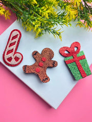 Festive Arendelle Christmas Glitter Hair Pins styled on a white tile with pink background, showcasing candy cane, gingerbread man, and gift box.