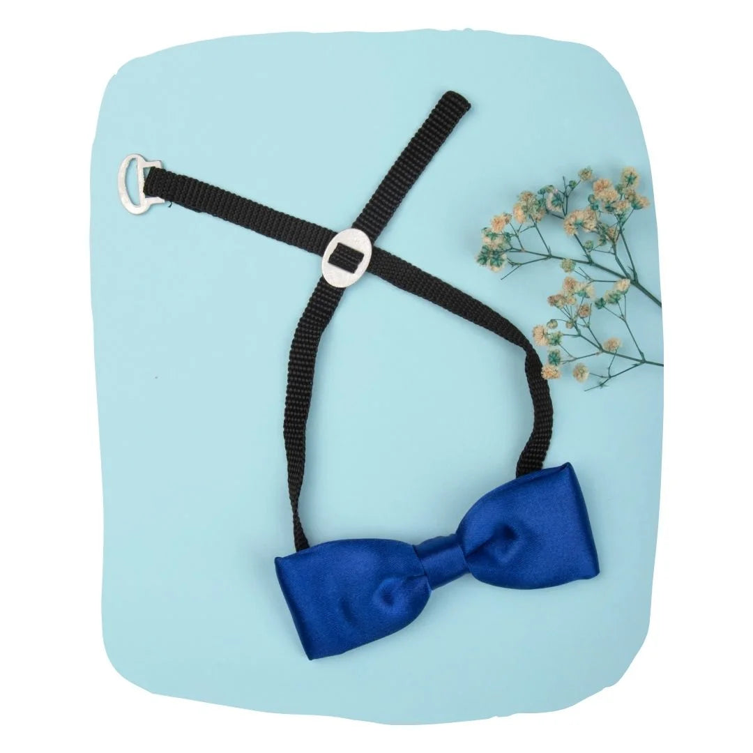 Adjustable ink blue satin bow tie for boys with black strap and clip-on, styled on a pastel background with floral accent.