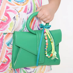 Close-up of green handbag featuring Fimo Bead Bag Charm - Green Ribbon Bow; vibrant beads and bow enhance bag appeal.