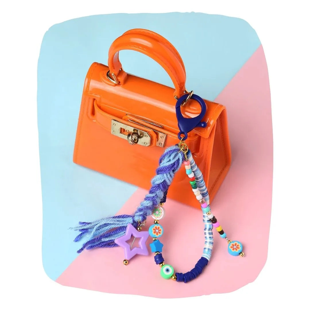 Blue Fimo Bead & Star Bag Charm clipped to a small orange handbag, showcasing its colorful beads and braided yarn strands.