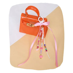 Beaded bag charm with pink hearts, smiley beads, and ribbon bow clipped to an orange mini handbag. Fun accessory for kids' backpacks or purses.