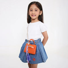 Young girl wearing a denim skirt and white top, carrying an orange handbag with a beaded bag charm for kids. Stylish and personalized accessory.