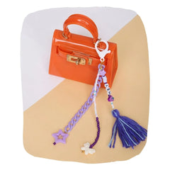 Beaded bag charm for kids clipped to an orange mini handbag, featuring purple beads, tassels, and a star charm. Fun backpack accessory for girls.