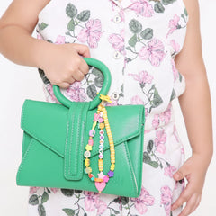 Close-up of a green handbag with a personalized orange bag charm for kids, showcasing vibrant beads, stars, and a heart pendant.